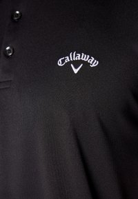 Černé polo tričko vyrobené z hladkého materiálu, s tříknoflíkovou légou. Vyšitý logo "Callaway" se nachází na levé straně hrudi.
