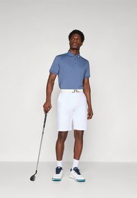 Ανδρικό πόλο πουκάμισο σε ανοιχτό μπλε, με κοντά μανίκια και γιακά, συνδυασμένο με λευκή βερμούδα. Αξεσουάρ περιλαμβάνουν λευκή ζώνη και μπαστούνι του γκολφ.