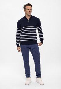 Marineblauwe trui met witte horizontale strepen, ritskraag, in combinatie met blauwe broek en witte sneakers. Glad textuur, aansluitend ontwerp.