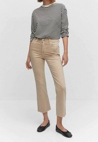 Camisa de rayas de manga larga en crema y negro, combinada con jeans cortos de color beige claro con dobladillos deshilachados, usados con bailarinas negras.