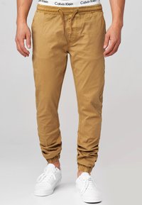 Pantalones jogger color arena con cintura elástica y cordón, que cuentan con puños elásticos en los tobillos. Fabricados en tejido suave, con bolsillos laterales.