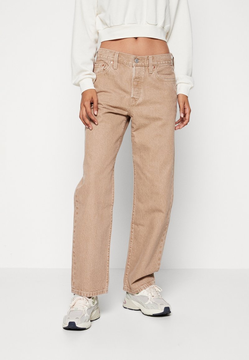 Pantalones vaqueros de mezclilla beige con pernera recta, bolsillos delanteros y cierre de botones, combinados con un sudadera corta blanca y zapatillas.