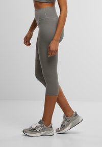 Grå høytalende capri leggings laget av glatt, elastisk materiale. Kombinert med grå treningsko med hvite detaljer og lisser.