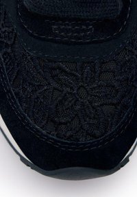 Zapatillas negras con una superposición de encaje floral, acentos de ante, una superficie texturizada y una suela blanca en contraste. Diseño curvado en la punta.