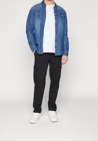 Blauwe denim overhemd met knopen en twee borstzakken, gecombineerd met zwarte cargobroek met zijzakken, en witte sneakers.