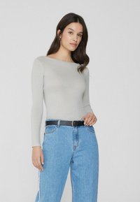 Haut à manches longues côtelé gris clair avec une encolure bateau, associé à un jean en denim bleu taille haute et une ceinture noire.