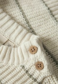 Strikket kremhvit genser med ribbestrikket krage, med teksturert stoff, grønne striper og to dekorative treknapper på skulderen.