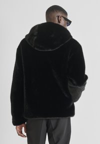 Crna jakna od umjetnog krzna s kapuljačom, mekane teksture, udobnog kroja i podvrnutih rukava. Ima glatku završnu obradu i ugodnu unutrašnjost.