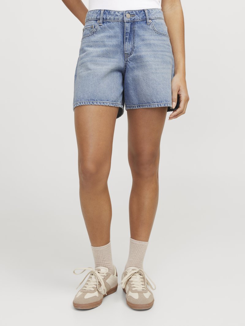 Shorts en denim bleu clair avec taille haute, comportant cinq poches, une fermeture à bouton et une coupe droite. Portés avec des baskets beiges et des chaussettes.