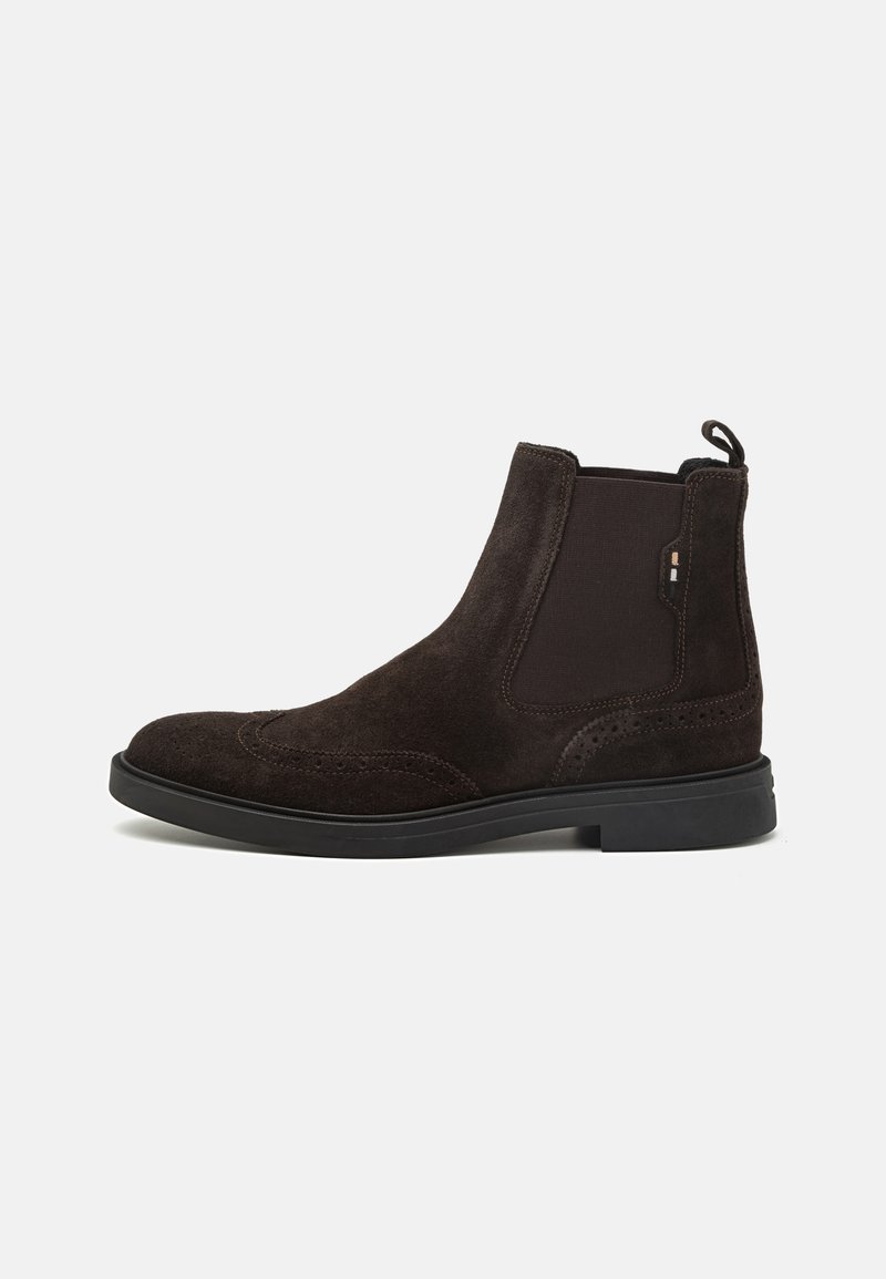 Botine Chelsea din suede maro, cu panouri laterale elastice, detalii perforate și o talpă din cauciuc negru contrastantă. Buclă în spate pentru o utilizare ușoară.