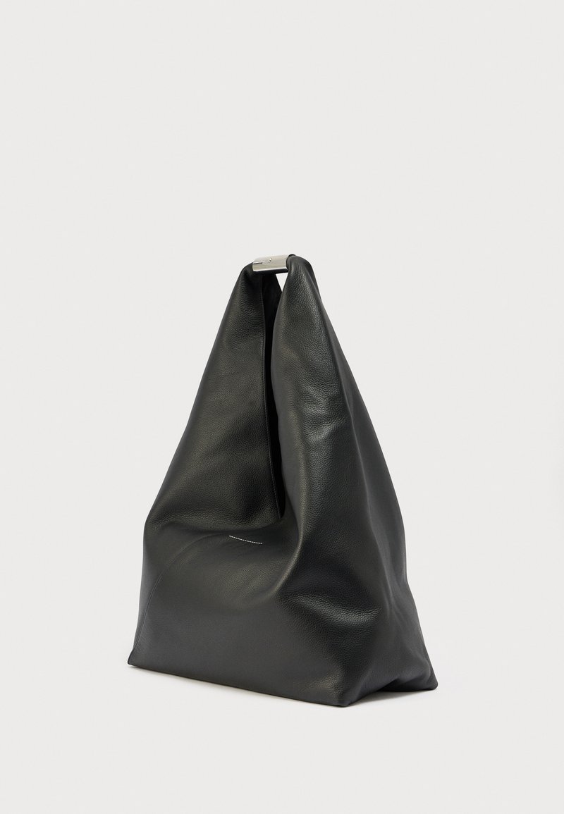 Sac fourre-tout en cuir souple noir avec une forme triangulaire et un fermoir en métal argenté en haut, posé sur un fond blanc uni.