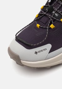 Chaussures violettes avec un dessus texturé, une marque GORE-TEX, une semelle grise et des accents de lacets réfléchissants avec des attaches jaunes.