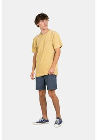 Camiseta de algodón amarilla de manga corta con un bolsillo en el pecho, combinada con pantalones cortos navy y zapatillas azules. Diseño sencillo y relajado.