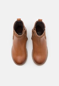 Botas de cuero marrón hasta el tobillo con puntera redonda, suela cosida y paneles laterales elásticos. Textura suave con un acento en tono bronceado en la parte trasera.