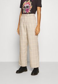 Beige rutiga högmidjade byxor med vida ben och framfållar, kombinerat med en svart grafisk t-shirt och svarta snörboots.