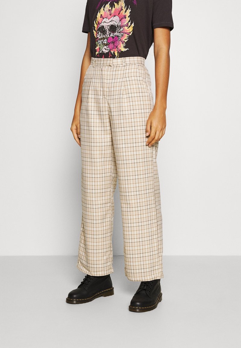 Beige rutiga högmidjade byxor med vida ben och framfållar, kombinerat med en svart grafisk t-shirt och svarta snörboots.