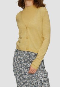 Yellow button-up cardigan over a ribbed mustard top, paired with a patterned skirt featuring a floral design in blue, white, and yellow tones.