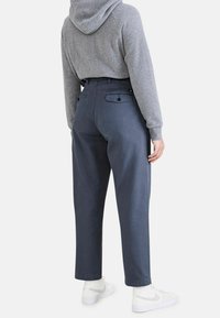 Mörkgrå byxor med hög midja i denim, med smalnande ben, bakfickor med knappstängning, tillsammans med vita sneakers.