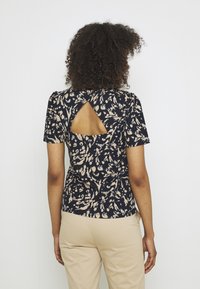 Laivastonsininen paita, jossa on vaaleanbeige kukkakuvio, lyhyet hihat ja avonainen leikkaus selässä. Sileä kangas ja istuva siluetti.