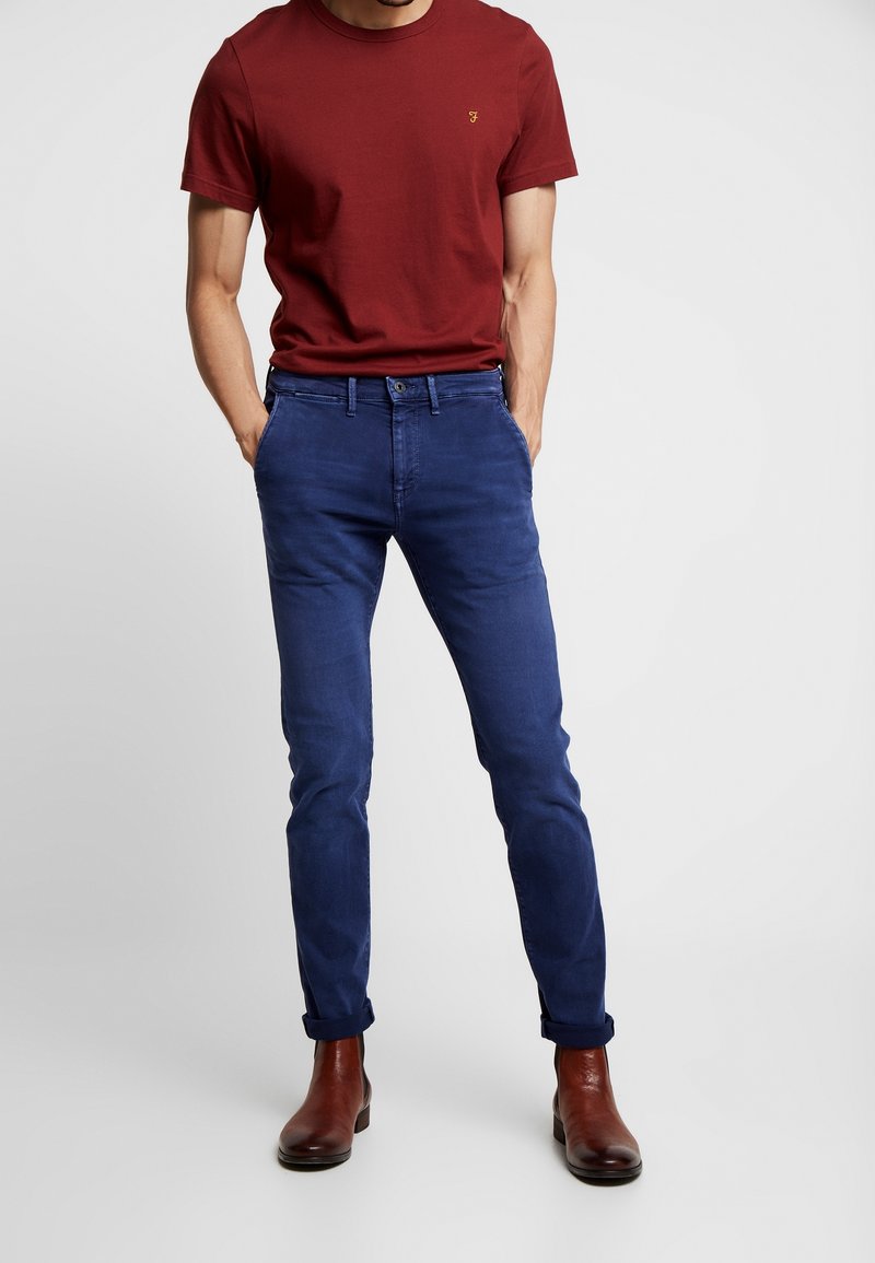 Röd bomulls-T-shirt med korta ärmar och en liten logotyp, ihop med blå slim-fit chinos och bruna läderankelstövlar.