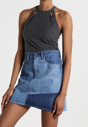 Débardeur côtelé gris foncé avec des bretelles distinctives, associé à une jupe en denim patchwork comprenant des sections allant du bleu clair au bleu foncé et un design ajusté.