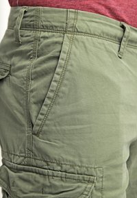 Olivově zelené, lehké šortky s plochým předním dílem, viditelným švem a bočními kapsami. Vyrobeno z měkké, odolné tkaniny.