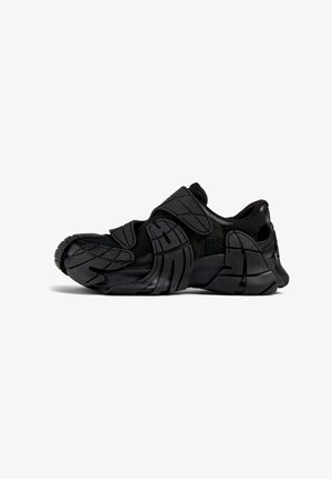 Black athletic shoe featuring a textured design with layered synthetic panels, a cushioned midsole, and a rounded toe.