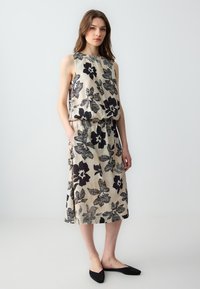 Beige en zwarte jurk zonder mouwen met bloemenpatroon, voorzien van een geraffineerde tailleband en zijzakken. Soepele stof met een ontspannen pasvorm.