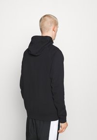 Svart huvtröja med en slät yta, figursydd design och ribbade ärmmuddar. Har en enkel, minimalistisk stil utan synliga logotyper.