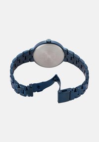 Modra kovinska ura s okroglo površino in nerjavečim jeklom na hrbtni strani. Povezave imajo gladko površino in vključujejo zaponko za prilagoditev.