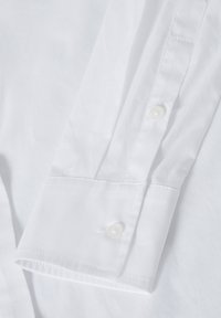 Camisa de vestir blanca de algodón con puño de un botón, textura suave y líneas limpias con detalles de costura precisos.