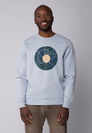 Hellblaues Sweatshirt mit einem Grafikdesign eines Schallplatten mit gelbem Zentrum und dunkelblauem Außenkreis, der ein strukturiertes Muster zeigt.