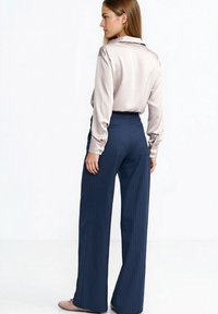 Jasnobeżowa satynowa bluzka z długimi rękawami i kołnierzykiem, zestawiona z granatowymi spodniami w prążki. Bluzka jest wpuszczona w spodnie z wysokim stanem.
