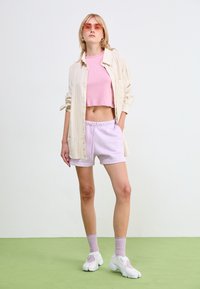 Lightweight cream striped shirt over a pink crop top, paired with lilac shorts and white sneakers. Model wears pink sunglasses and light socks.