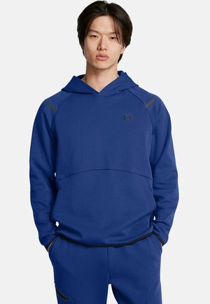 Sudadera azul marino con un bolsillo tipo canguro, acentos negros en los hombros, un escote amplio y un logo sutil en el pecho. Textura de tela suave.