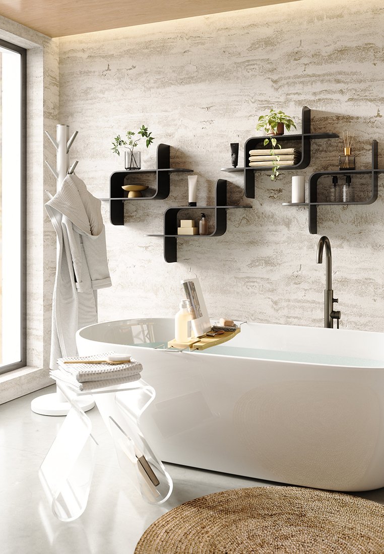 Vasca da bagno bianca a libera installazione in un bagno moderno con parete in pietra, mensole galleggianti nere sovrapposte, uno sgabello in acrilico trasparente e un tappeto intrecciato.