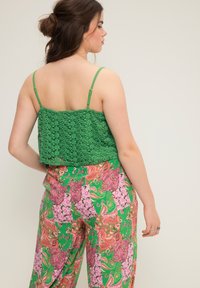 Grön spets crop top med tunna axelremmar, i kombination med färgglada, mönstrade vida byxor med paisley- och blommönster i rosa och grönt.
