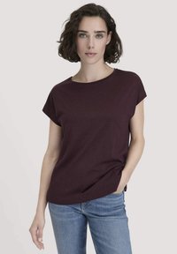 Burgunderfarbenes Kurzarm-T-Shirt mit rundem Ausschnitt, aus weichem Baumwollstoff, kombiniert mit hellblauen Jeans. Glatte Textur, lockere Passform.