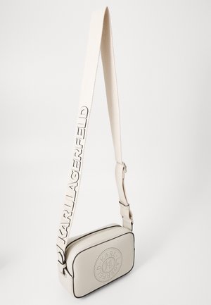 Kremowa, prostokątna torba na ramię z okrągłym perforowanym logo i szerokim paskiem z dużymi literami nazwy marki KARL LAGERFELD.