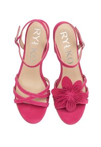 Różowe zamszowe sandały z paskiem wokół kostki, wplecionym wzorem oraz dekoracyjnym kwiatem na palcu. Płaska podeszwa o gładkim wykończeniu.