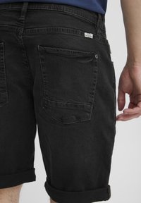 Șorturi din denim negre cu manșete răsucite, având două buzunare pe spate și un mic eticheta a mărcii. Textură netedă și croială lejeră.