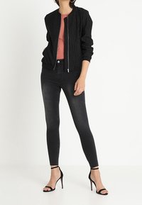 Czarna bomberka w paski, dopasowana, z prążkowanymi mankietami. Noszona na różowej bluzce, w połączeniu z czarnymi rurkami i czarnymi sandałkami na szpilce.