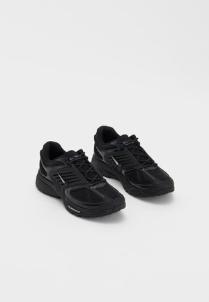 Sapatos desportivos pretos com um upper em malha texturizada, apresentando um sistema de atacadores e detalhes refletivos. Solas de borracha grossa para maior tração.