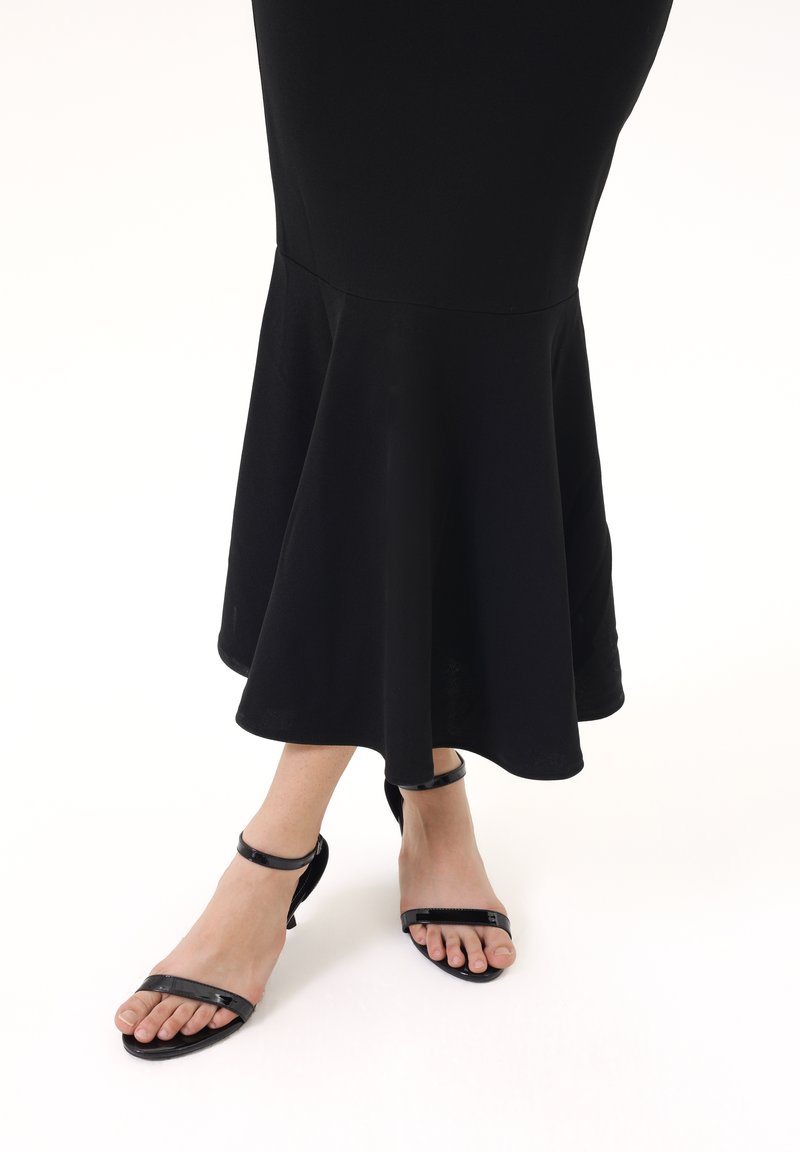 Czarna, rozkloszowana sukienka o gładkiej fakturze; zestawiona z czarnymi sandałami na płaskiej podeszwie i paskami na kostce.