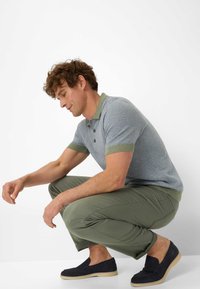 Polo a maniche corte di colore blu con un design a motivi, colletto verde, abbinato a pantaloni verde oliva e scarpe nere senza lacci.