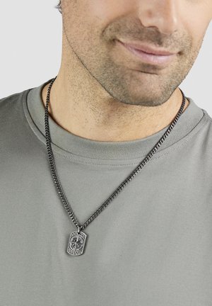 Mann trägt graues Hemd und silberne Kettenhalskette mit Kompassanhänger, Nahaufnahme des Halses und unteren Gesichts.