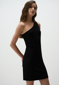 Abito nero a coste con design a spalla unica, silhouette aderente e lunghezza sopra il ginocchio. Texture liscia con dettagli minimi.