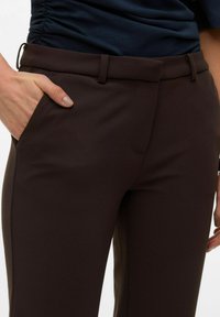 Brune skreddersydde bukser med en jevn tekstur, med en sidelomme og et flatt livbånddesign. Stoffet virker lett.