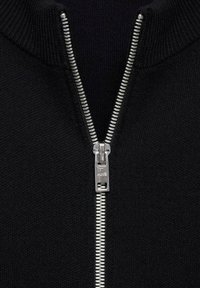 Crna zip-up dukserica s metalnim srebrnim patentnim zatvaračem, rebrastim ovratnikom i teksturiranim materijalom. Šavovi su minimalni s čistim linijama.