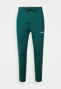 Zelené sportovní kalhoty s elastickým pasem a stahovací šňůrkou. Mají boční kapsu a bílý nápis "PEGADA" podél nohy. Hladká textura.